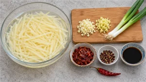 Julienned potato strips soaking in cold water beside garlic, ginger and Sichuan seasonings