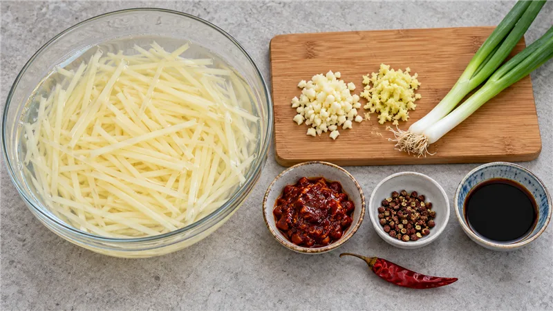 Hot And Sour Shredded Potatoes: Sichuan Recipe and Tips 2 Julienned potato strips soaking in cold water beside garlic, ginger and Sichuan seasonings