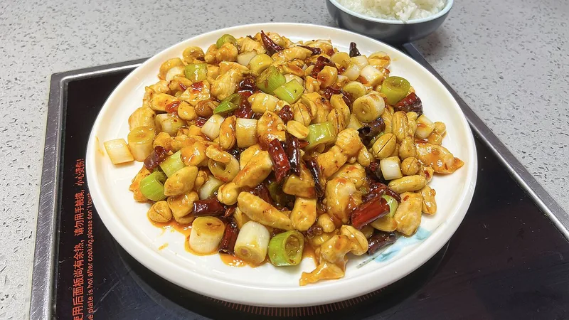 Kung Pao Chicken Recipe Sichuan Style: Heat, Sauce, and Peanut Texture Checks 1 Cooked chicken cubes with peanuts, scallion sections and dried chili on a white plate beside rice