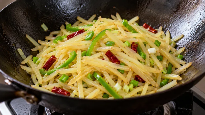 Julienned potatoes with green pepper, dried chili and scallion in a wok