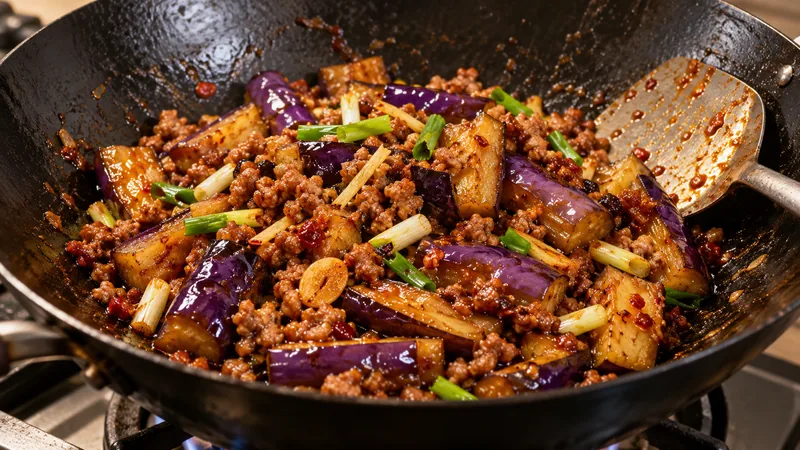 Sichuan Eggplant Recipe: Sauce, Texture, and Timing Checks 3 Cooked eggplant pieces with browned fine pork mince, ginger, garlic and scallion in a black wok