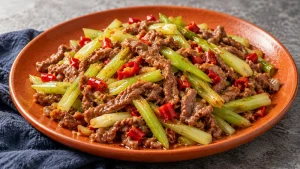 Tender beef shreds and pale-green celery with red pickled pepper pieces on an orange ceramic platter