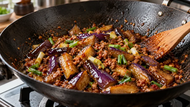 Fish Fragrant Eggplant Recipe: Sauce Ratio, Texture, and Wok Timing 3 Tender seared eggplant and cooked minced pork simmering in glossy doubanjiang sauce with scallions in a black wok