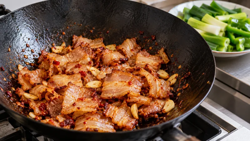 Twice Cooked Pork Recipe: Slicing, Sauce, and Wok Timing Checks 2 Thin cooked pork belly slices seared with doubanjiang and garlic in a wok, with leek and green pepper waiting nearby