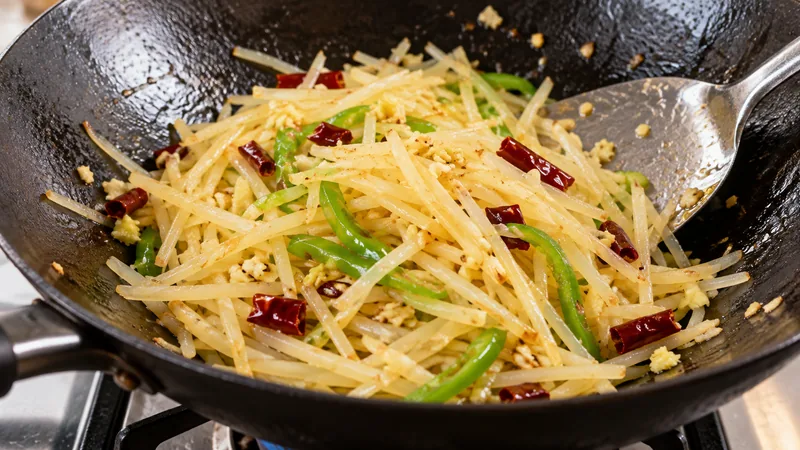Sichuan Shredded Potatoes Recipe: Cutting, Acidity, and Wok Timing 2 Thin potato and green pepper shreds being stir-fried in a wok