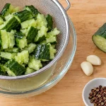 Cold Mixed Cucumber: Sichuan Recipe and Home Cooking Tips 1 Smashed raw cucumber draining in a colander over a glass bowl